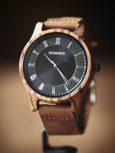 Botanica watch with brown leather strap black face with roman numerals set in a wooden case.