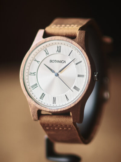 Botanica watch with brown leather strap silver face with roman numerals set in a wooden case.