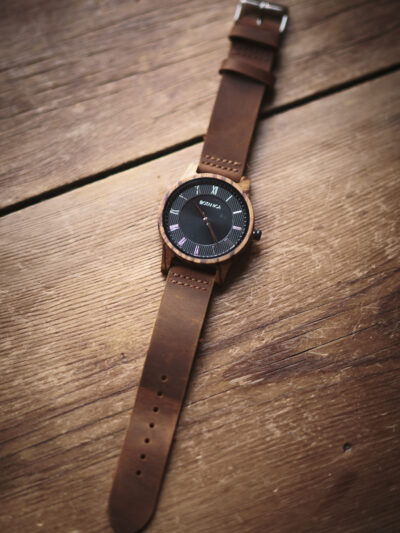 Botanica watch with brown leather strap black face with roman numerals set in a wooden case.