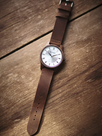 Botanica watch with brown leather strap silver face with roman numerals set in a wooden case.