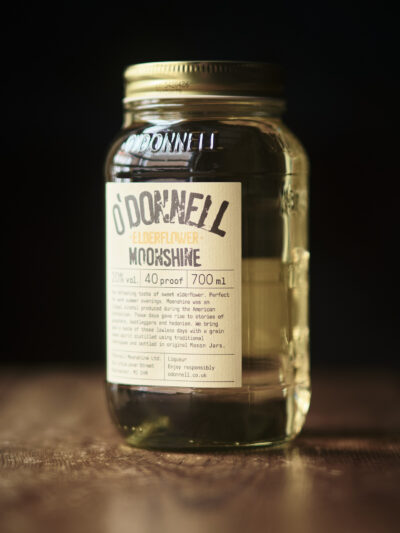 A jar of Elderflower Moonshine, light golden liquid in a mason jar with vintage style label.