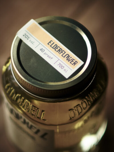 A jar of Elderflower Moonshine, viewed from above. Light golden liquid in a mason jar with vintage style label.