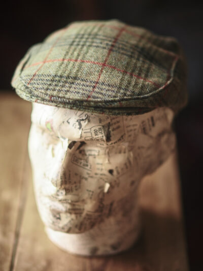 A model head wearing a traditional green flat cap
