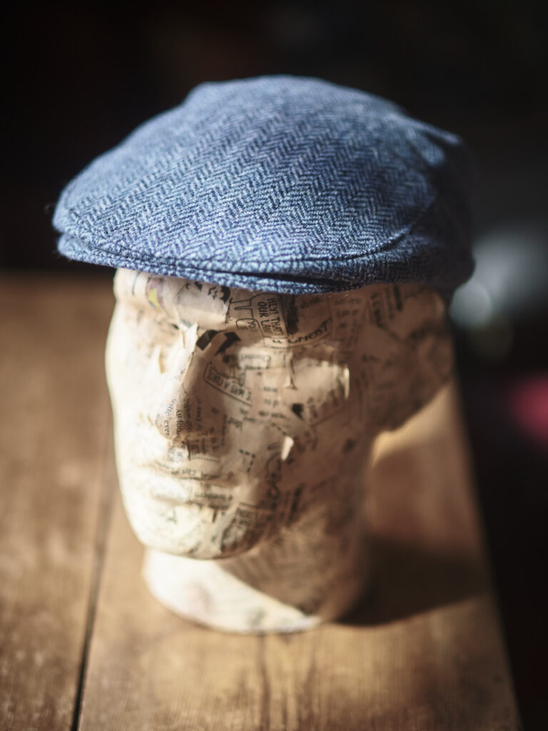 A model head wearing a traditional blue flat cap