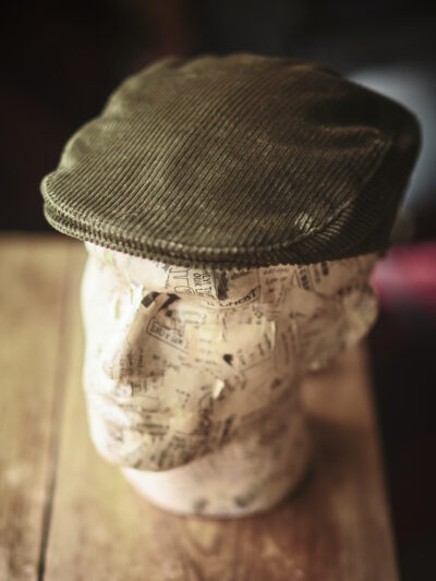 A model head wearing a traditional green corduroy flat cap