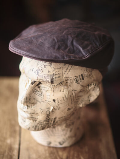 A model head wearing a traditional brown waxed flat cap